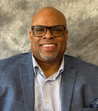 Man with bald head and salt and pepper goatee wearing a navy blazer over white button up shirt