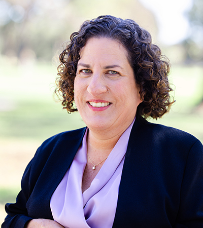 Woman with short curly hair wearing a purple blouse and navy suit jacket